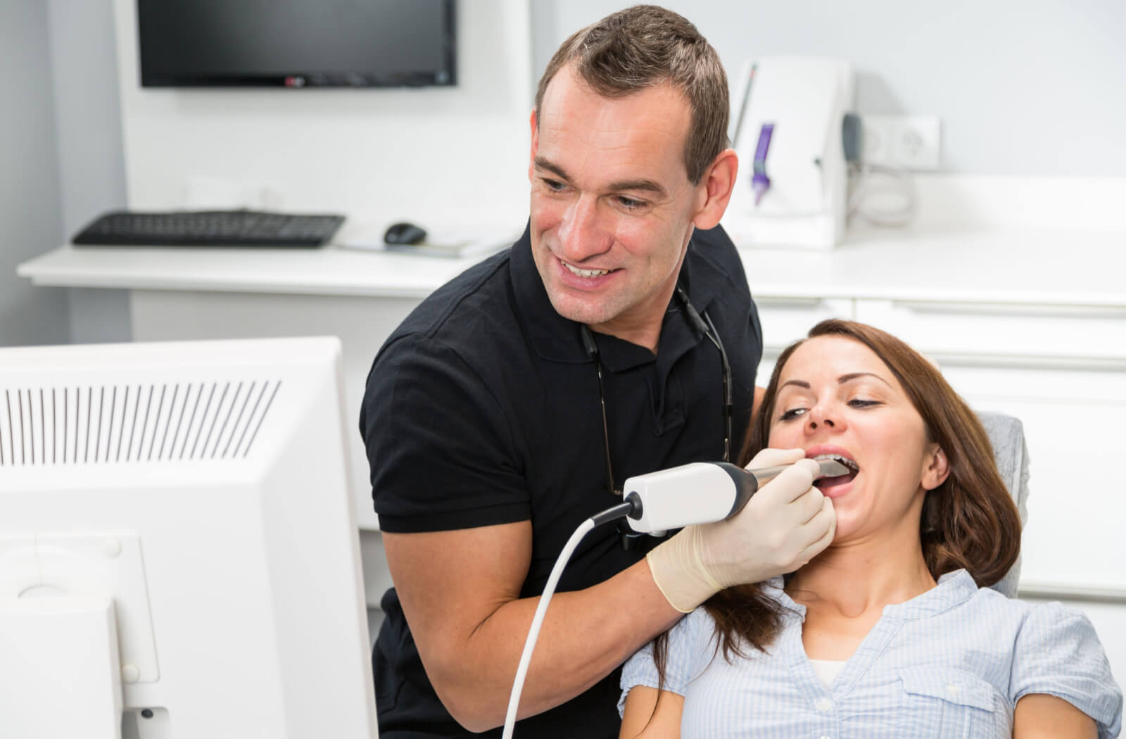 A male dentist scanning patient's teeth with CEREC (Chairside Economical Restoration of Esthetic Ceramics) scanner,