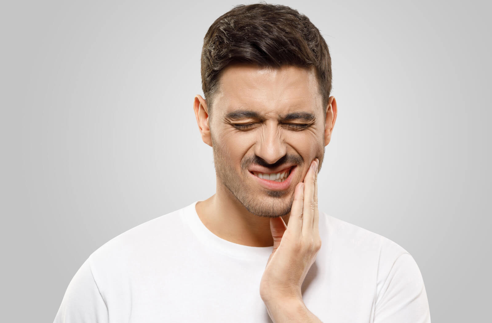 A man suffering from a toothache holding his left cheek with his left hand.